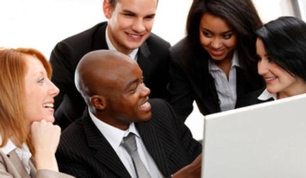 A diverse group of five smiling colleagues working together, looking at a laptop screen.