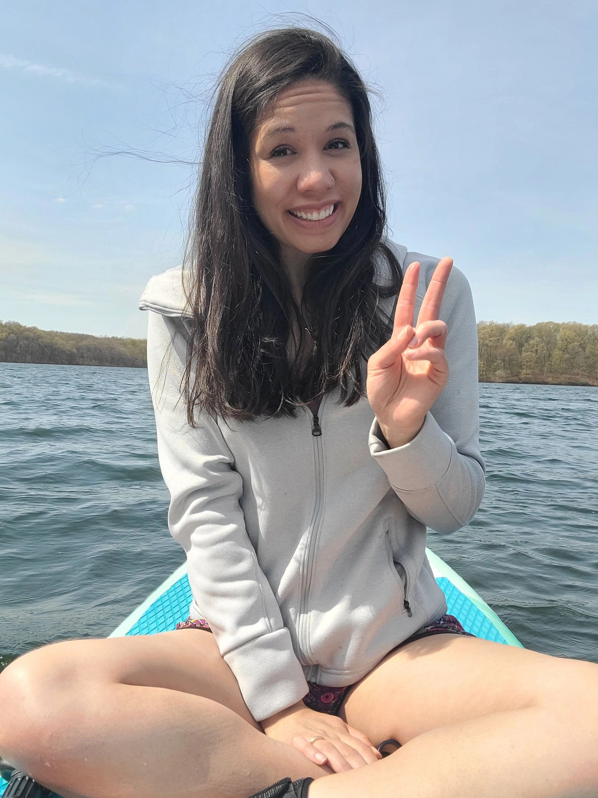 Smiling woman on a paddleboard showing peace sign on a sunny day.