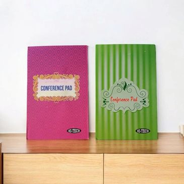 Two colorful conference pads on a wooden surface, one pink and one green.