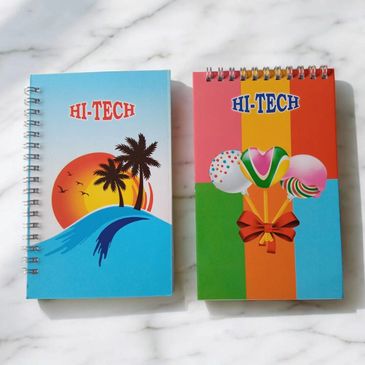 Two colorful HI-TECH spiral notebooks with vibrant covers on a marble surface.
