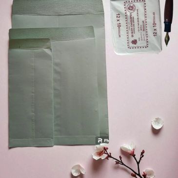 Three envelopes, a pack of envelopes, a wooden pen, and cherry blossom petals on a pink background.