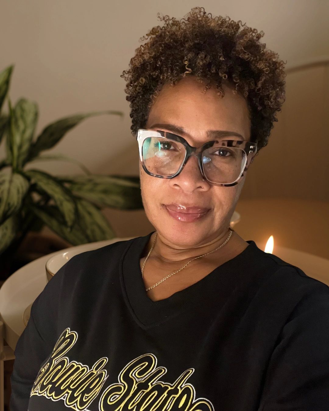 Woman with curly hair and glasses taking a selfie.