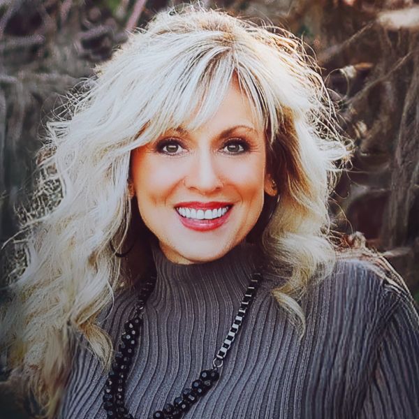 Smiling woman with blonde hair and a gray sweater outdoors.