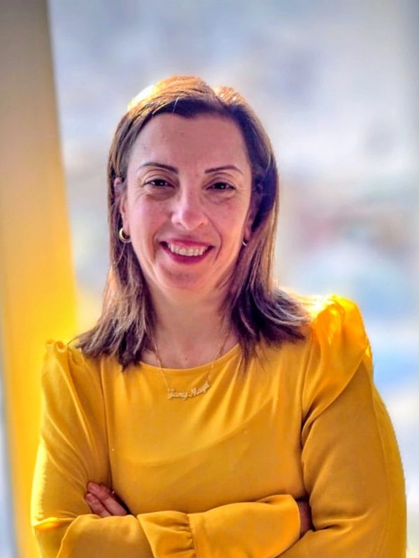 Woman in a yellow blouse smiling with arms crossed in soft natural light.