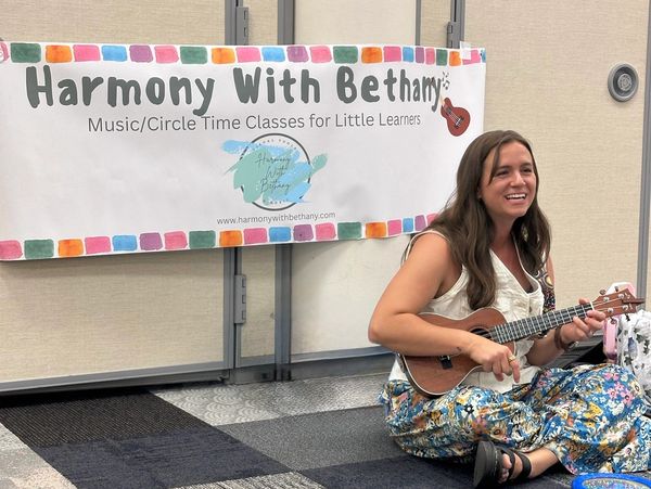 A woman happily plays a ukulele during a music class for little learners.