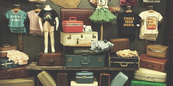 A vintage display of suitcases and children's clothing on mannequins.