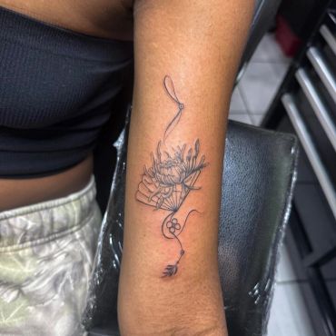 Delicate flower tattoo with flowing line art on a forearm.