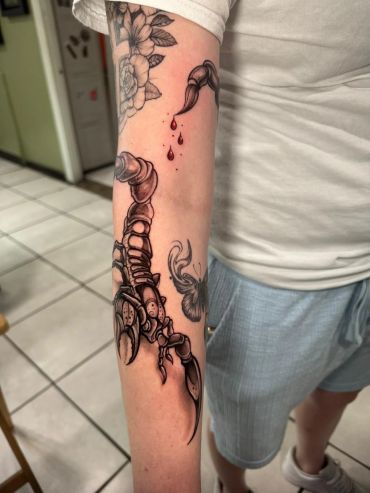 Detailed scorpion tattoo with a flower and blood drops on the forearm.