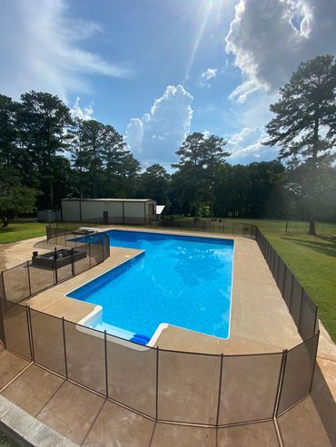 Outdoor swimming pool surrounded by safety fencing on a sunny day.