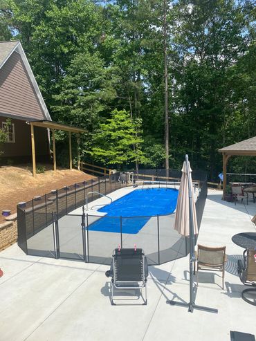 Backyard pool with safety fence, lounge chair, and umbrella on a sunny day.