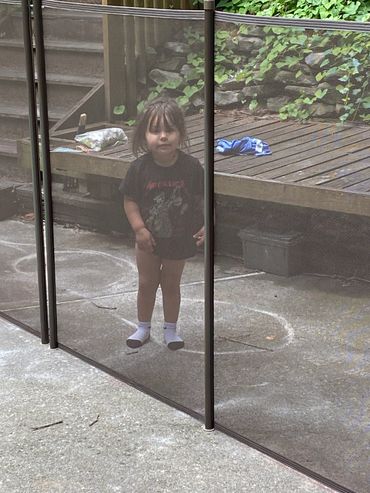 Young child standing behind a mesh screen outdoors in casual clothes.