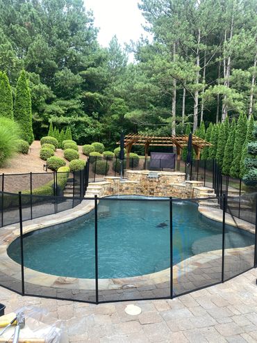 Serene backyard pool with safety fence and lush greenery.