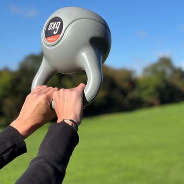 Person lifting a gray kettlebell outdoors on a sunny day.