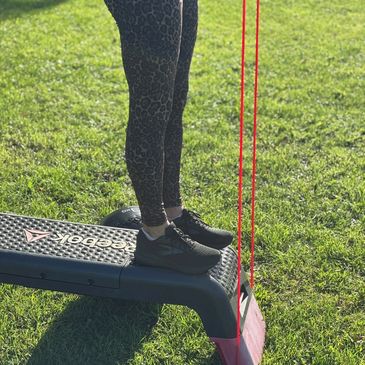Person standing on a fitness step platform with resistance bands outdoors.