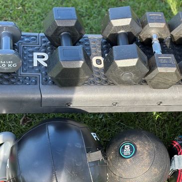 Various dumbbells and weighted balls on a rack outdoors.