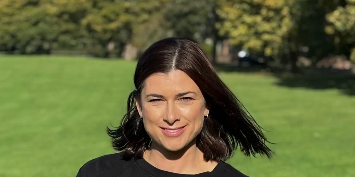 Woman with dark hair smiling outdoors on a sunny day.
