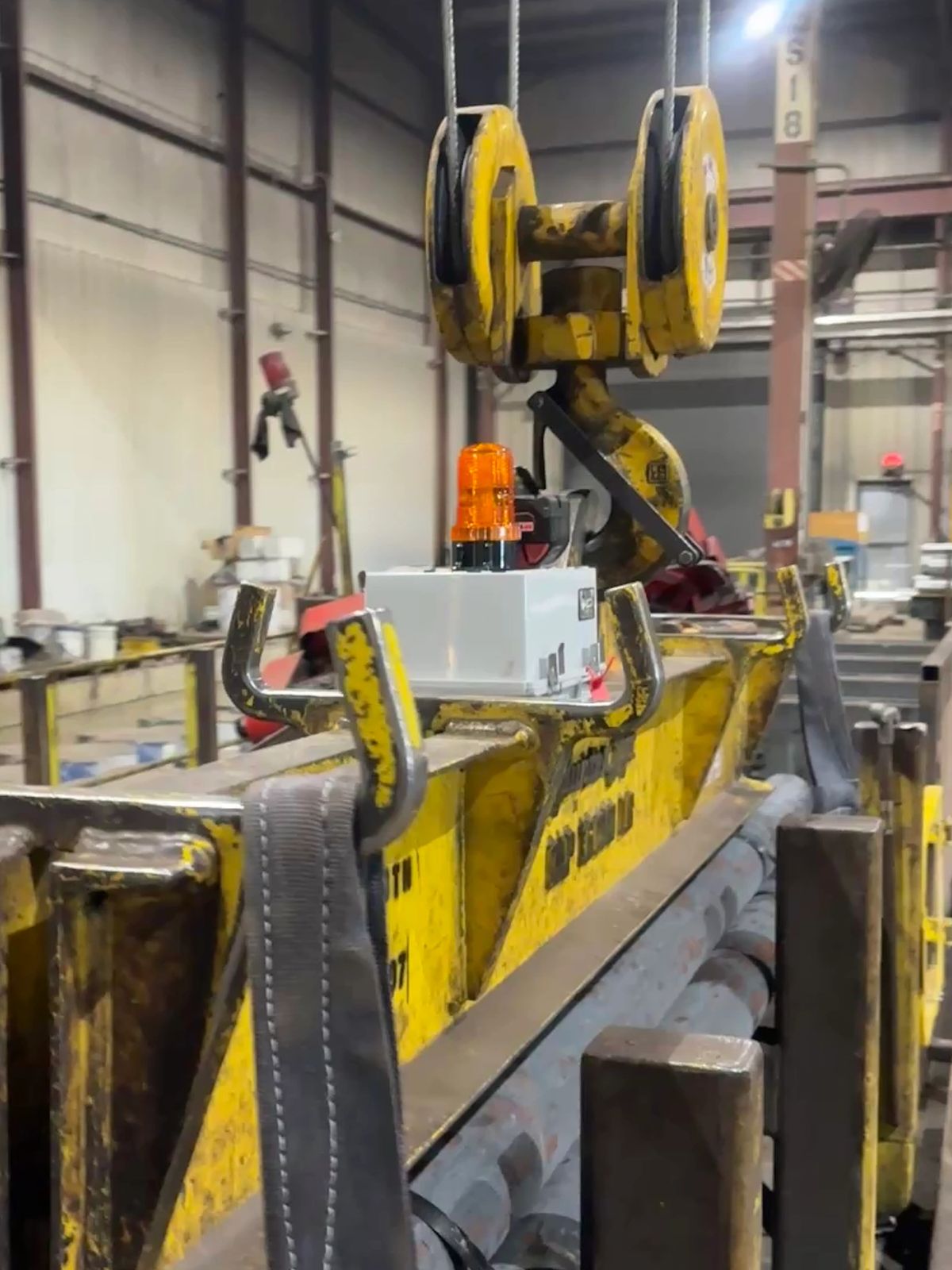Yellow industrial lifting hook with safety light in a warehouse setting.