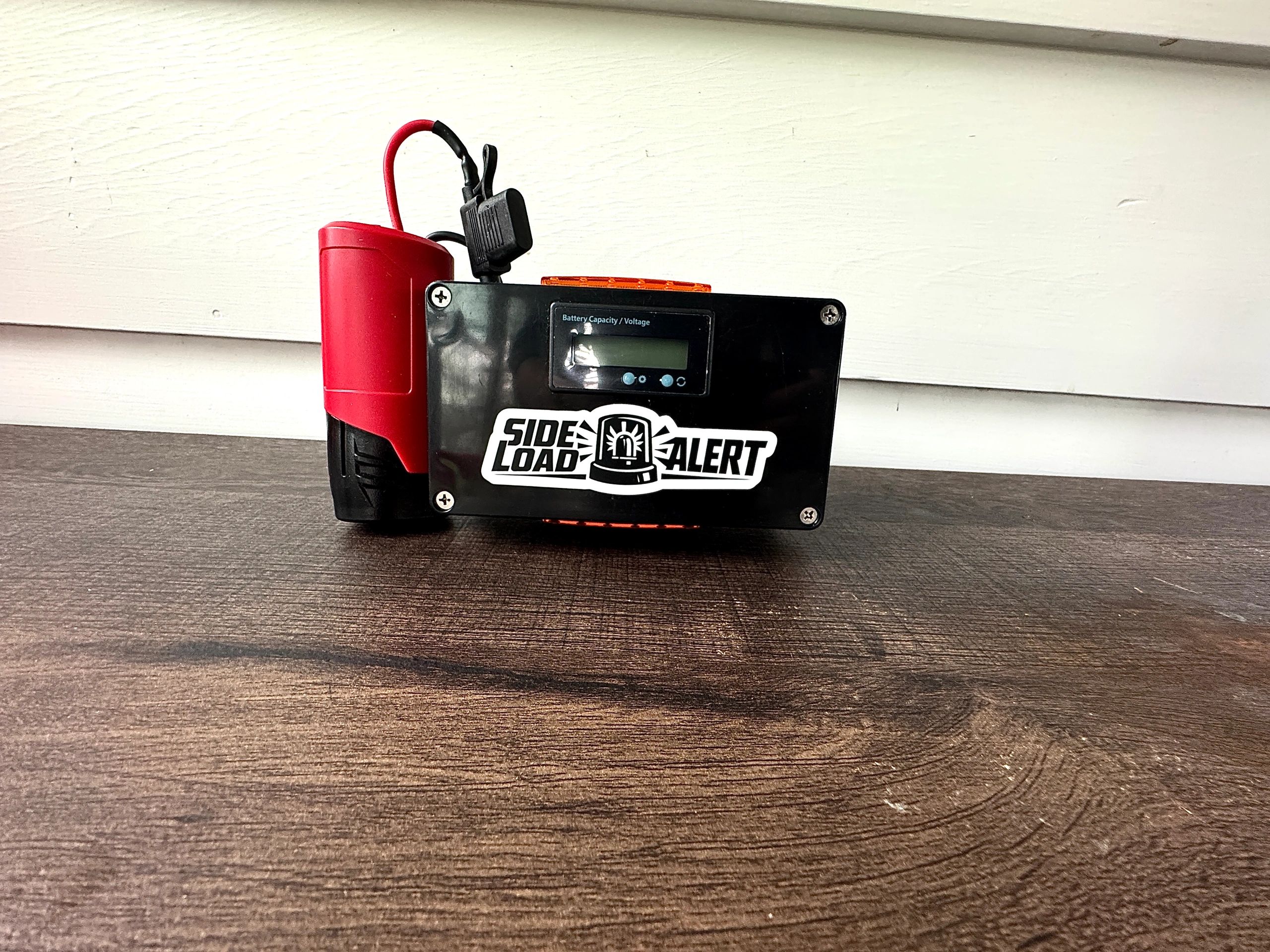 A Side Load Alert device with a digital screen and red components on a wooden surface.