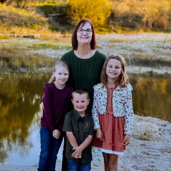 Woman with three smiling children by a lake.
