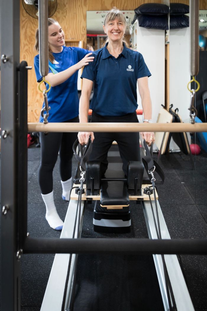 A physio guiding a patient on a Pilates reformer