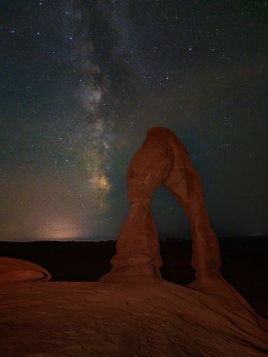 Milky Way over a natural rock arch at night.