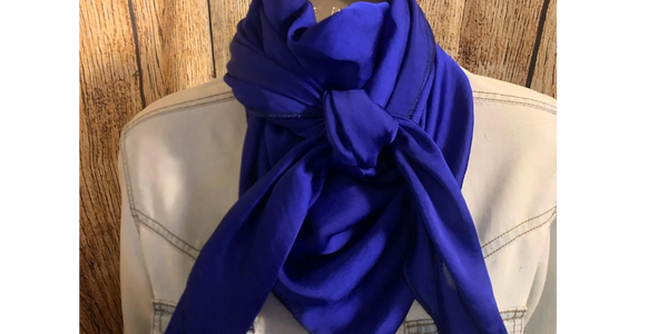 Bright blue scarf tied stylishly on a white jacket against a wooden background.
