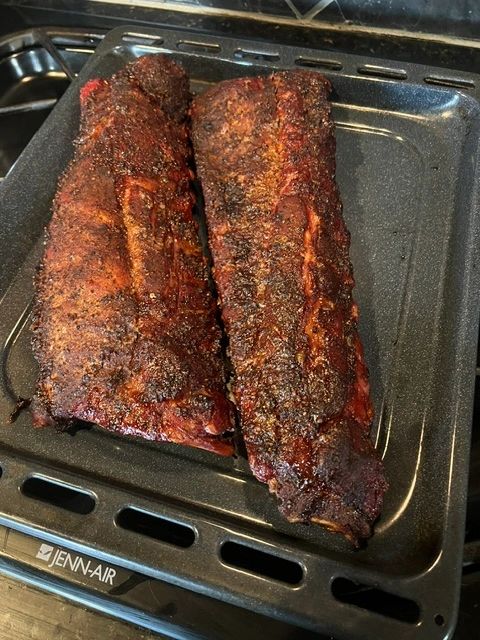 Two slabs of seasoned, cooked ribs on a black baking tray.