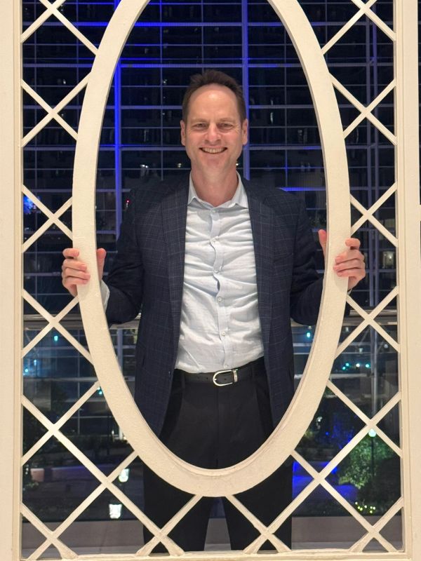 Man smiling through an oval frame at night.