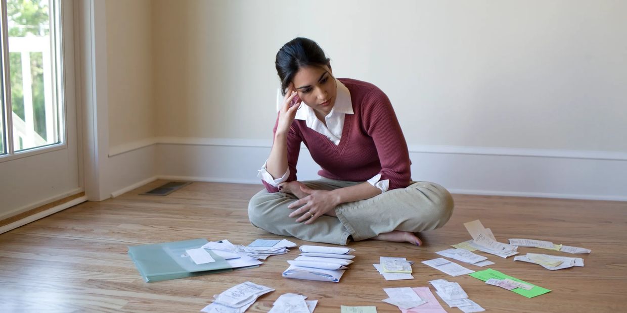 A woman sitting on the floor, looking worried while sorting papers.