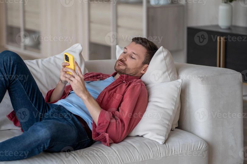 Man relaxing on a couch while using a smartphone.