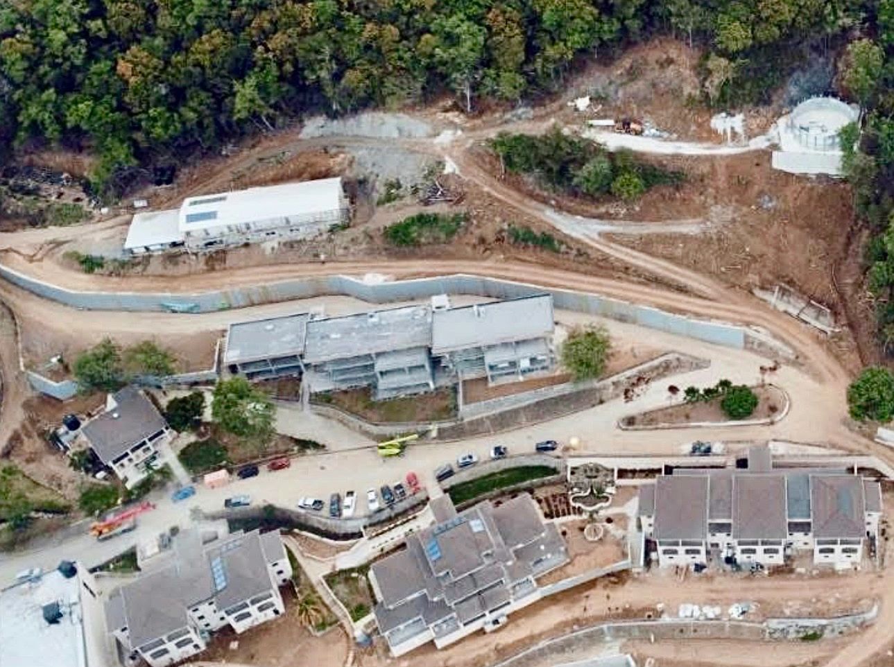 Aerial view of a construction site surrounded by trees with multiple buildings and vehicles.