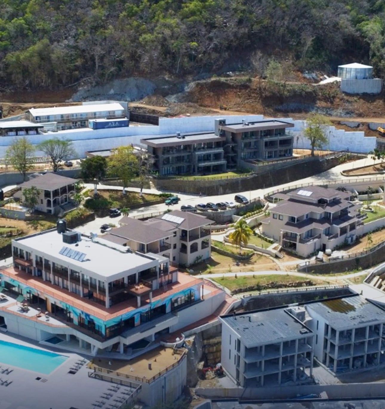 A large residential complex with multiple buildings and a swimming pool on a hillside.