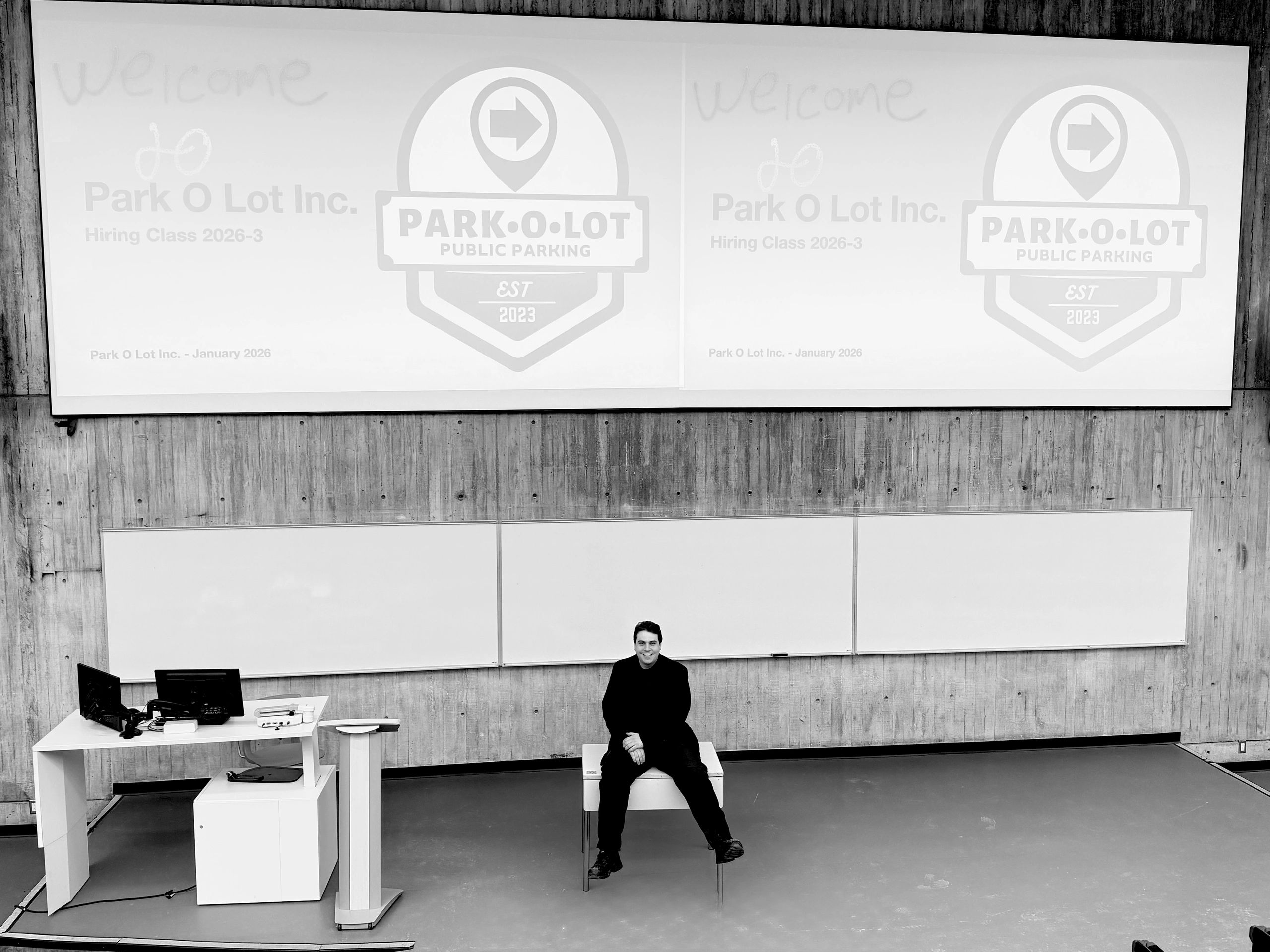 Man sitting in a large lecture hall with a projector screen.