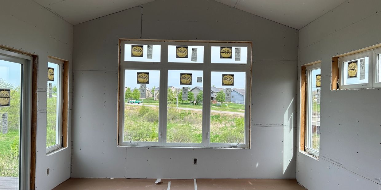 Room under construction with large windows and drywall.