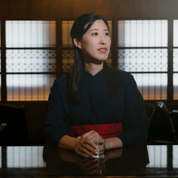 Woman in traditional attire holding a glass, sitting contemplatively.