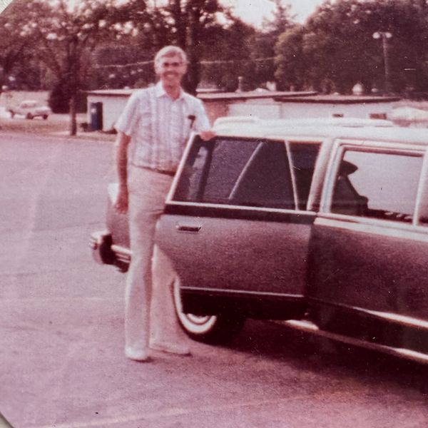 Man standing next to a vintage car in a parking lot.
