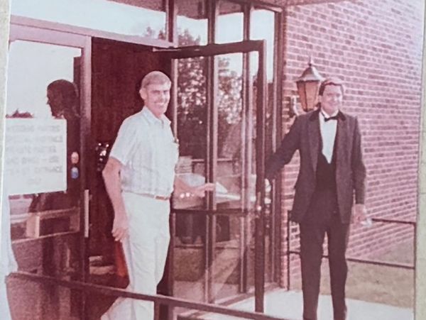 Two men at a glass door, one holding it open for the other.