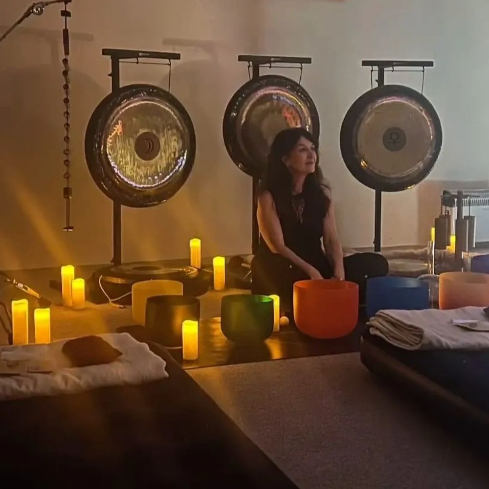 Woman sitting among gongs and glowing candles in a calming space.