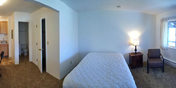 Simple bedroom with bed, chair, and lamp near a window.