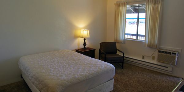 Simple bedroom with a bed, chair, lamp, and window.