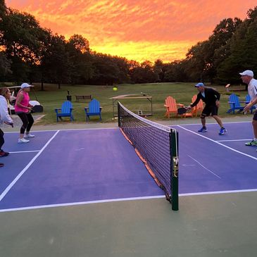 People playing pickleball on an outdoor court during a vibrant sunset.