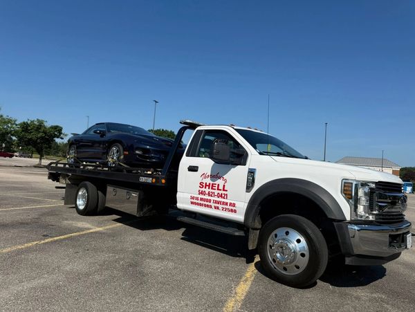 A white tow truck carrying a black sports car in a parking lot.