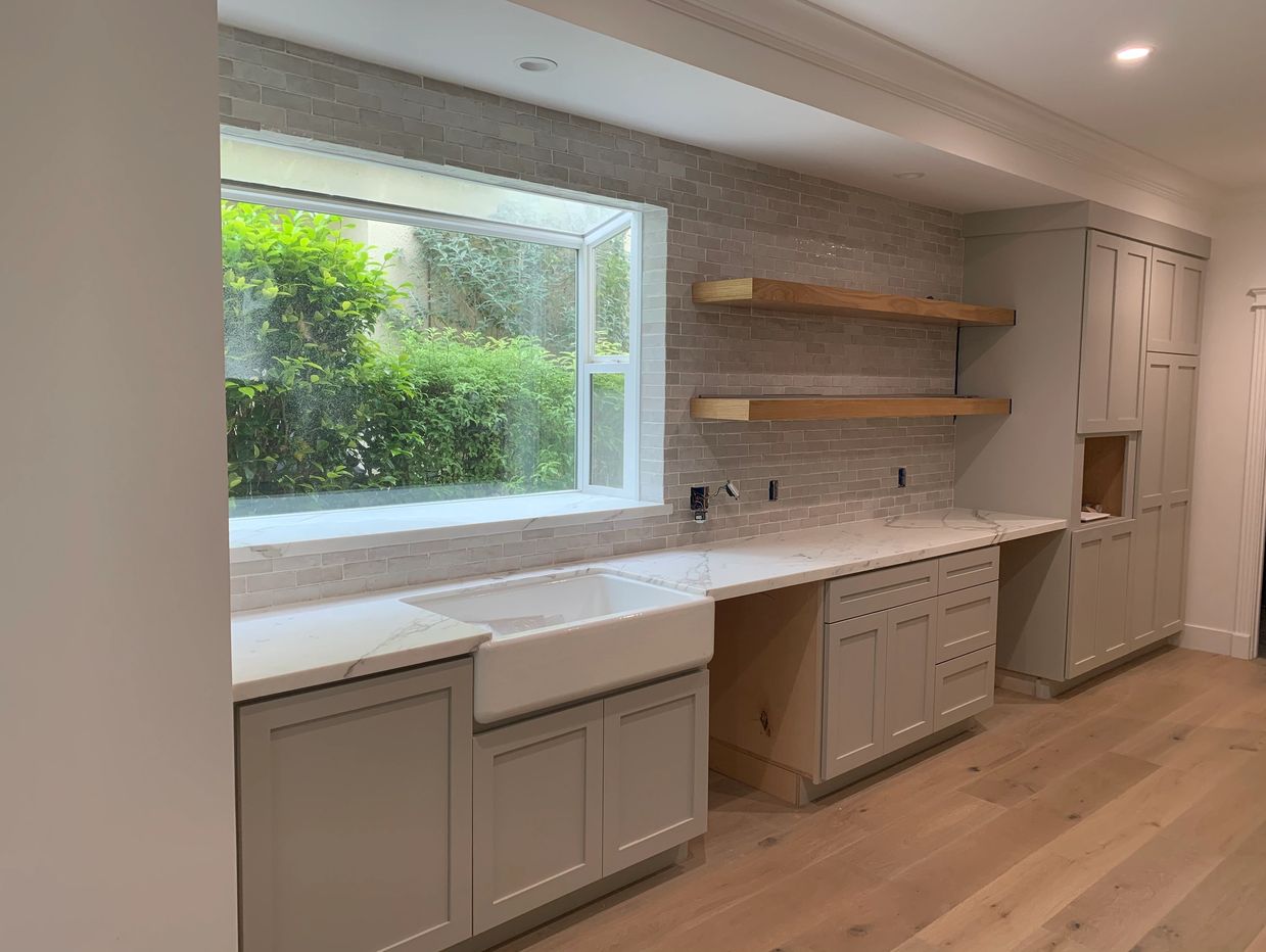 Custom shaker cabinets with farmhouse sink. Full wall tile back splash and oak floating shelves. 
