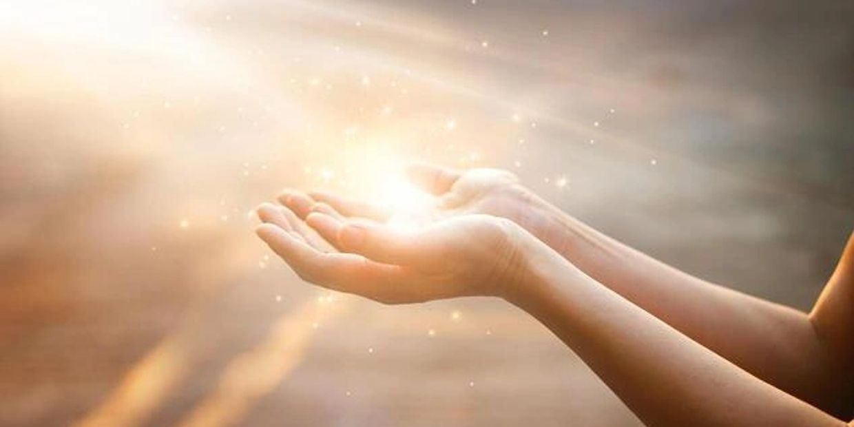 Hands holding glowing light with sparkles.