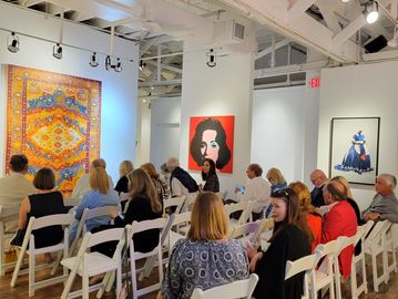 People seated in an art gallery with colorful paintings on walls.