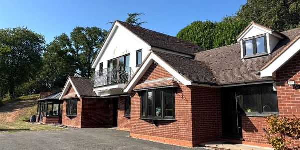 Spacious brick house with black windows and a balcony under a clear blue sky.