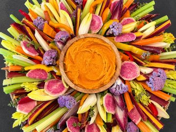 A vibrant, seasonal display of fresh, colorful vegetables beautifully arranged around a creamy house