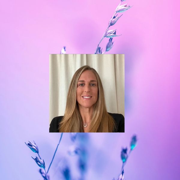 Smiling woman with long blonde hair against a soft floral pink-purple background.