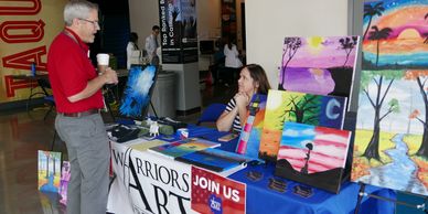 An art booth with colorful paintings and two people talking.