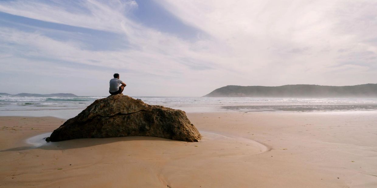 Man sitting by the ocean reflecting and taking time to manage difficult emotions
